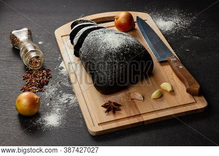 Fresh Black Rye Bread On A Cutting Board With Seasonings Sprinkled With Flour On A Black Wooden Tabl