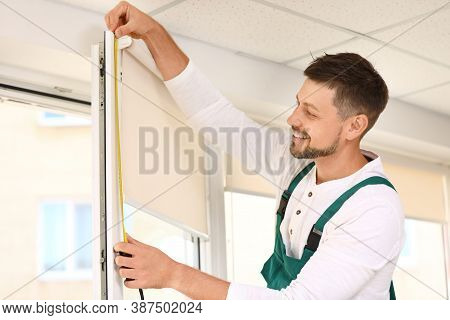 Handyman With Tape Measure Installing Roller Window Blind Indoors