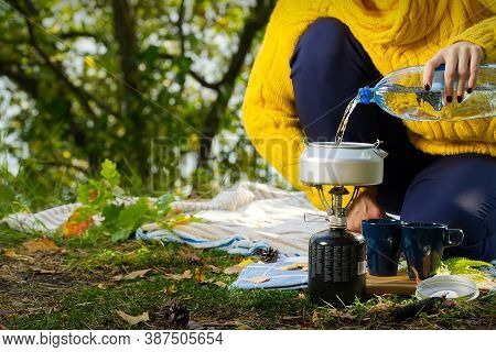 Young Beautiful Girl In A Yellow Sweater Makes Coffee In The Forest On A Gas Burner. Making Coffee O