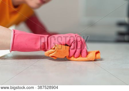 Cleaning The House. A Woman In Pink Rubber Gloves Diligently Wipes The Kitchen Countertop With A Rag