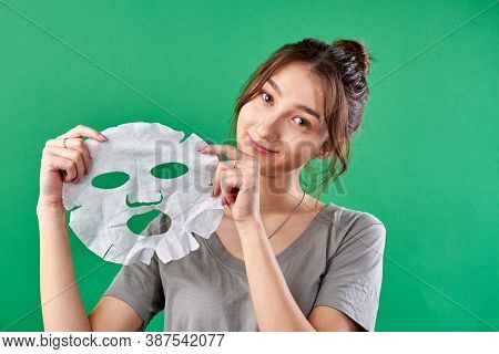 Portrait Of Young Woman Holding Spa Sheet Mask. Beauty And Skincare. Isolated On Green Chromakey Bac