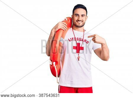 Young handsome man wearing lifeguard uniform holding float pointing finger to one self smiling happy and proud 