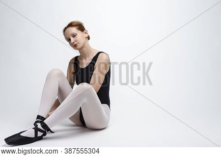 Portrait Of Positive Caucasian Ballet Dancer In Body Suit And Pointes Shoes Against White Background
