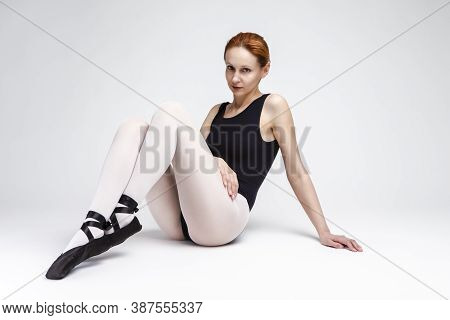 Caucasian Professional Ballet Dancer In Body Suit  And Pointes Shoes Posing Against White Background