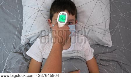 A Recovering Boy Medical Protective Mask Lying In Bed And His Mother Measuring Temperature With Infr