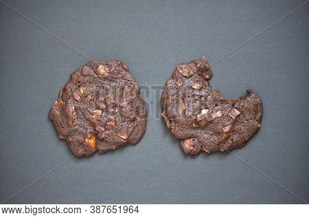 Close Up. Two Dark Brown Homemade Chocolate Cookies With Nuts On Black Background. One Piece Is Bitt