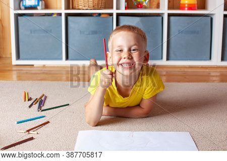 Cute Blond Boy Draws On Paper Lying On The Floor And Smiles. The Concept Of Educational Games, Extra