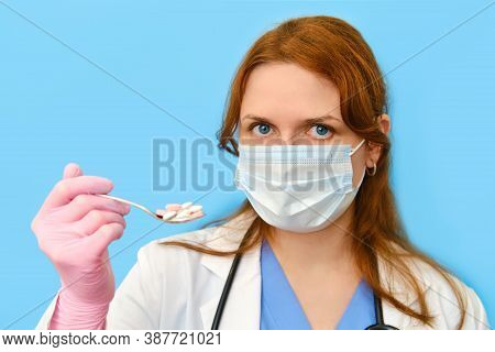 Doctor In A Medical Mask With A Spoon Of Pills In His Hand On A Blue Background, Portrait