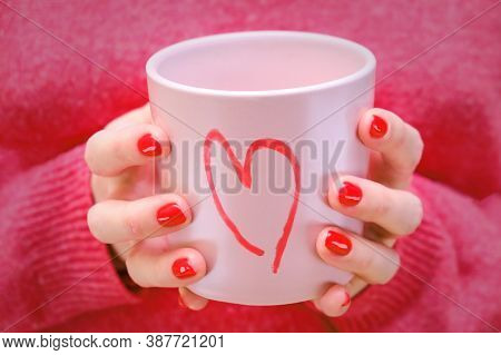 A Woman Holds A Pink Cup With A Painted Heart. The Girl In The Red Sweater With A Romantic Mug.
