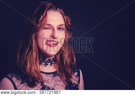 Red-haired Woman With Makeup For Halloween Ingratiatingly Licks Her Tongue Lips, Copy Space On A Bla