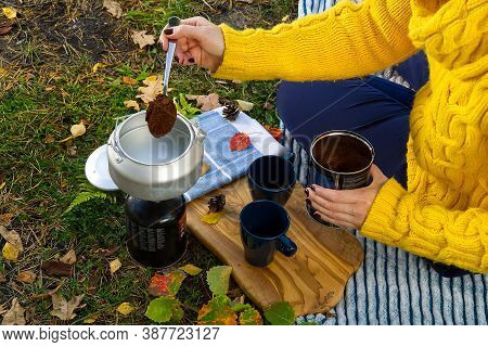 Young Beautiful Girl In A Yellow Sweater Makes Coffee In The Forest On A Gas Burner. Making Coffee O