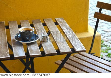 Espresso lungo coffee in a blue cup with milk in a little metal jug on a wooden table on a yellow wa