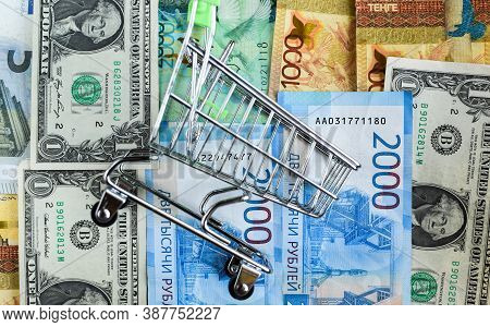 Russian Rubles, American Dollars, Euros, Kazakhstani Tenge Under An Empty Grocery Cart. Internationa