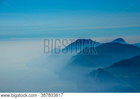 The Peaks Of The Alps Around Lake Garda Surrounded By Fog With Blue Sky Seen From Monte Altissimo, T