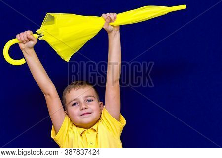 Attractive Surprised Caucasian Blond Schoolboy Holds Unexpanded Umbrella On Blue Studio Background.b