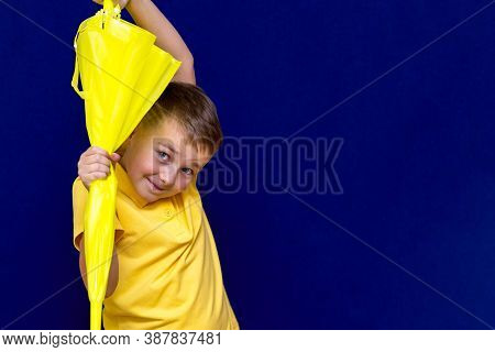 Attractive Surprised Caucasian Blond Schoolboy Holds Unexpanded Umbrella On Blue Studio Background.b