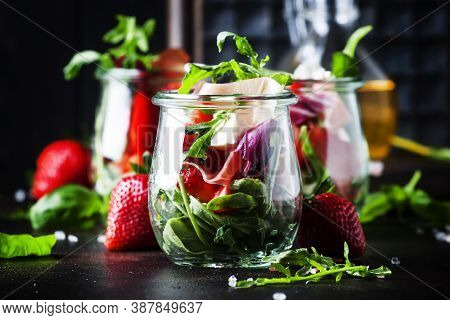 Summer Salad With Arugula, Soft Cheese, Red Strawberry And Prosciutto In Glass Jars On Black Table, 