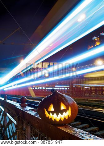 Halloween Pumpkin With A Glowing Grimace At Night On The Railway Bridge. In The Background There Are