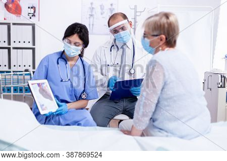 Cardiologist And Nurse Dicussing About Heart Disease With Senior Woman During Consultation And Givin