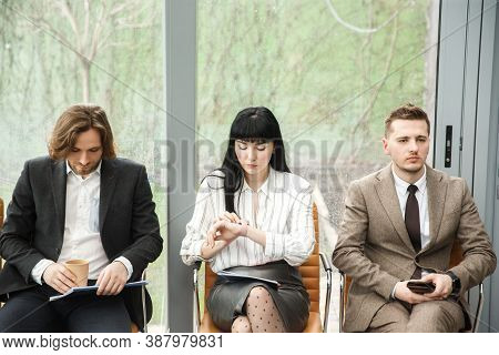 Three Office Workers Are Waitig For An Appointment. The Woman In The Middle Is Looking At Her Watch