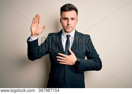 Young handsome business man wearing elegant suit and tie over isolated background Swearing with hand on chest and open palm, making a loyalty promise oath