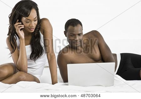 African American para za pomocą laptopa i telefon w sypialni