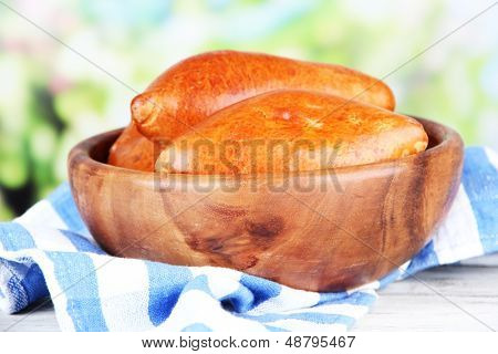 Empanadillas al horno frescos, en un recipiente de madera, en la mesa de madera, sobre fondo brillante