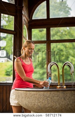 Young woman fillig a plastic bottle with healthy mineral water from a wellspring in a spa (shallow DOF)