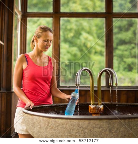 Young woman fillig a plastic bottle with healthy mineral water from a wellspring in a spa (shallow DOF)