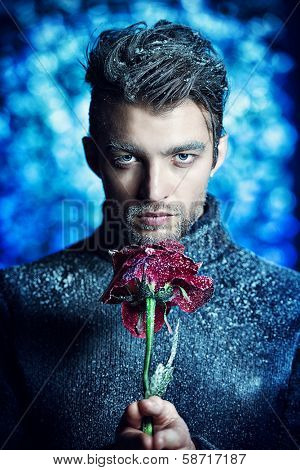 Portrait of a handsome man dressed in winter clothes, holding a rose, covered with snow.