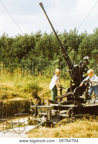 Vintage photo (scanned reversal film) of brother and sister playing in open air military museum (early eighties)