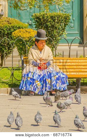 LA PAZ, BOLIVIA, MAY 8, 2014 - Local woman in traditional costume and bowler hat sits on bench on Plaza Murillo, watching pigeons