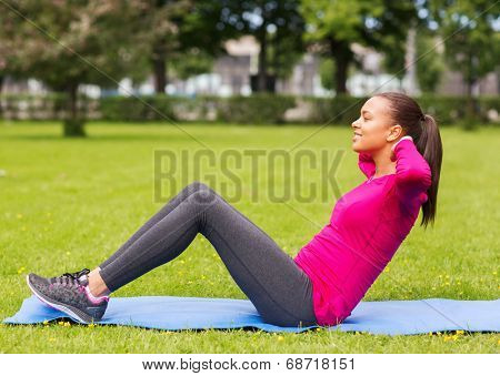 fitness, sport, training, park and lifestyle concept - smiling woman doing exercises on mat outdoors