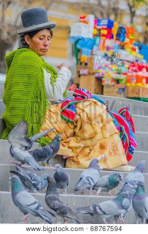 LA PAZ, BOLIVIA, MAY 9, 2014 - Local woman in traditional costume and bowler hat sits on stairs on Plaza Murillo, watching pigeons