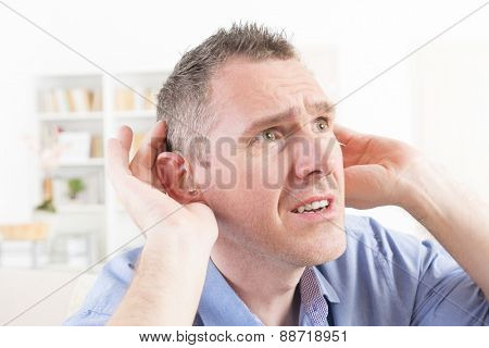 Man wearing deaf aid in ear attempting to hear something