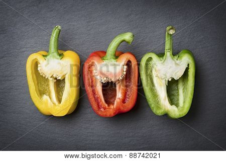 Arrangement with three colorful sweet peppers isolated on dark grey slate flagstone.