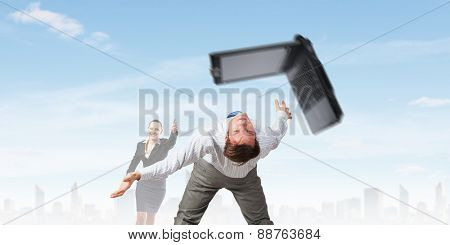 Young businessman trying to evade from thrown laptop