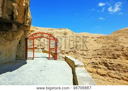 Decorative red gate with a cross on a mountain road going to the temple. Wadi Kelt near Jerusalem