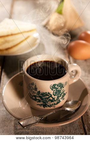 Steaming traditional oriental Chinese kopitiam style dark coffee in vintage mug and saucer with coffee beans. Fractal on the cup is generic print. Soft focus with dramatic light on wooden background.