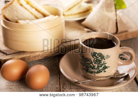 Steaming traditional oriental Chinese kopitiam style dark coffee in vintage mug and saucer with coffee beans. Fractal on the cup is generic print. Soft focus with dramatic light on wooden background.