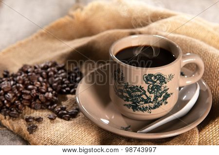 Steaming traditional oriental Chinese kopitiam style dark coffee in vintage mug and saucer with coffee beans. Fractal on the cup is generic print. Soft focus with dramatic light on wooden background.