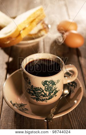 Steaming traditional oriental Chinese kopitiam style dark coffee in vintage mug and saucer with coffee beans. Fractal on the cup is generic print. Soft focus with dramatic light on wooden background.