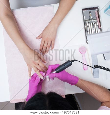 Hardware manicure. Removal of old gel varnish in the salon. Manicure master doing beauty procedure for client, closeup and top view