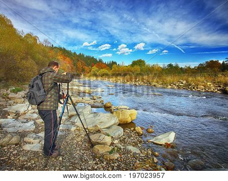 mountain river with stones in autumn forest with photographer. Dramatic sky