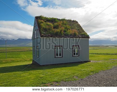 Glaumber - open-air folk museum - tradicional icelandic house with turf roof and white red windows with green grass and blue sky