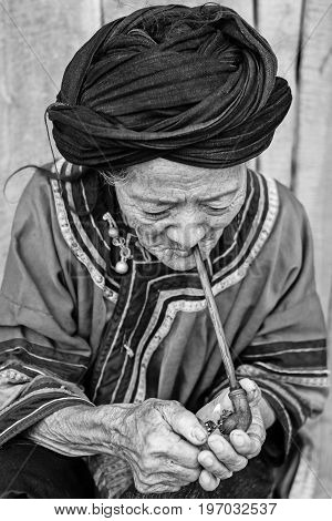 Phongsali Privince Laos - 25.July 2010: senior adult hill tribe woman in traditional clothes smoke her pipe