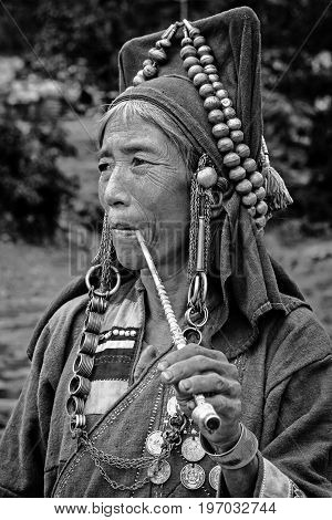 Phongsali Privince Laos - 24.July 2010: senior adult hill tribe woman in traditional clothes smoke her pipe