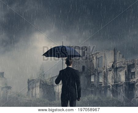 Businessman with umbrella standing over apocalyptic background. Crisis, default, setback concept.