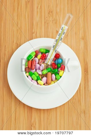 kop med flerfarvede tabletter og kapsler og hermometer
