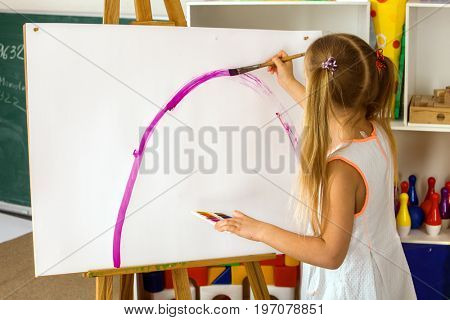 Children painting finger on easel. Group of kids girl and boy with teacher learn paint in class school. Child picture on background. Students draw a rainbow. Good psychological state of child.